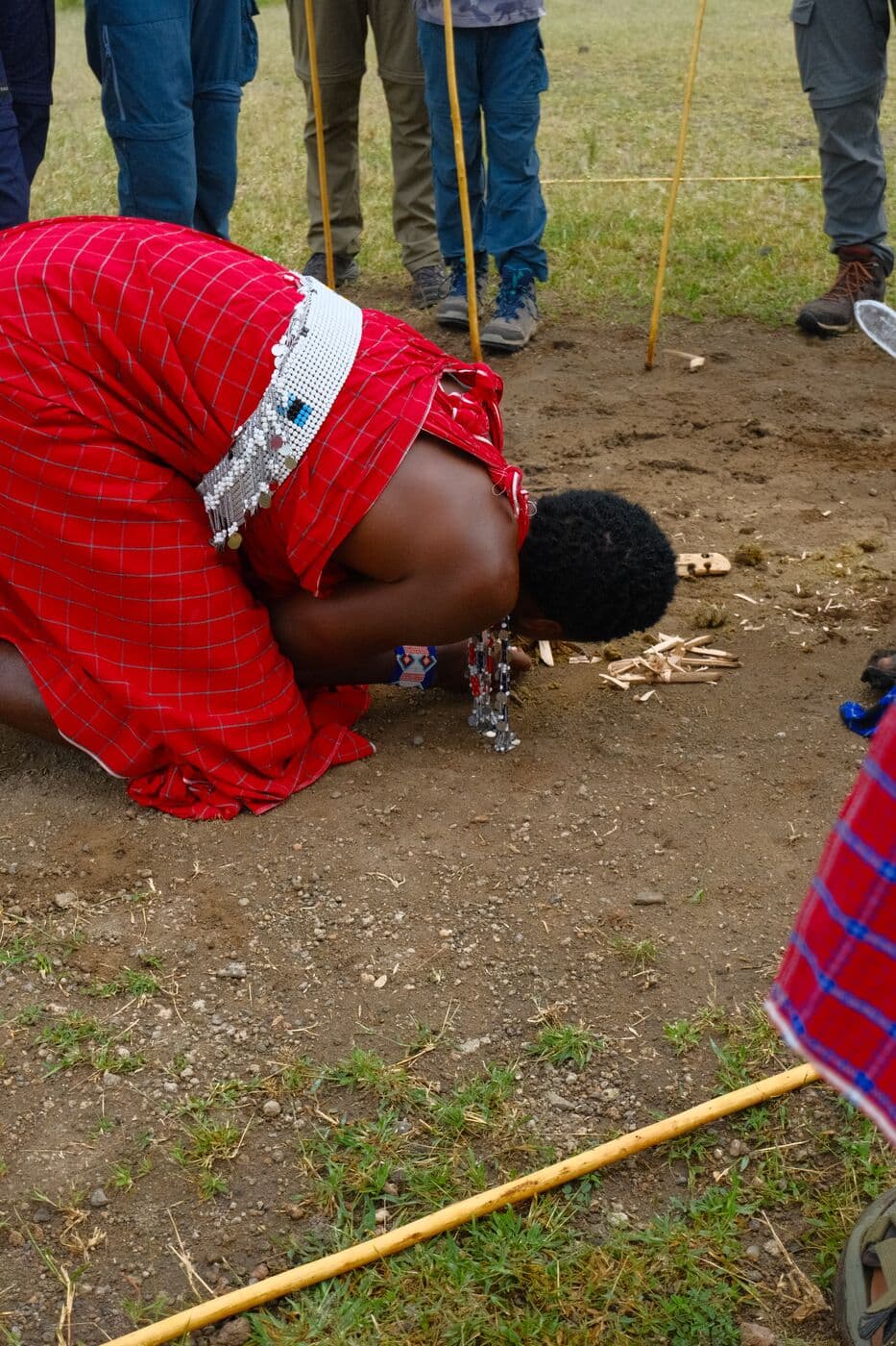 A Maasai woman in a red shuka bending to greet visitors.