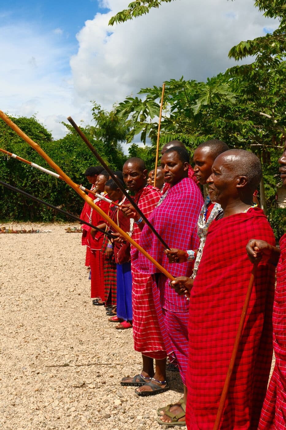 Maasai in beaded collars and red dress standing together beneath a tree.