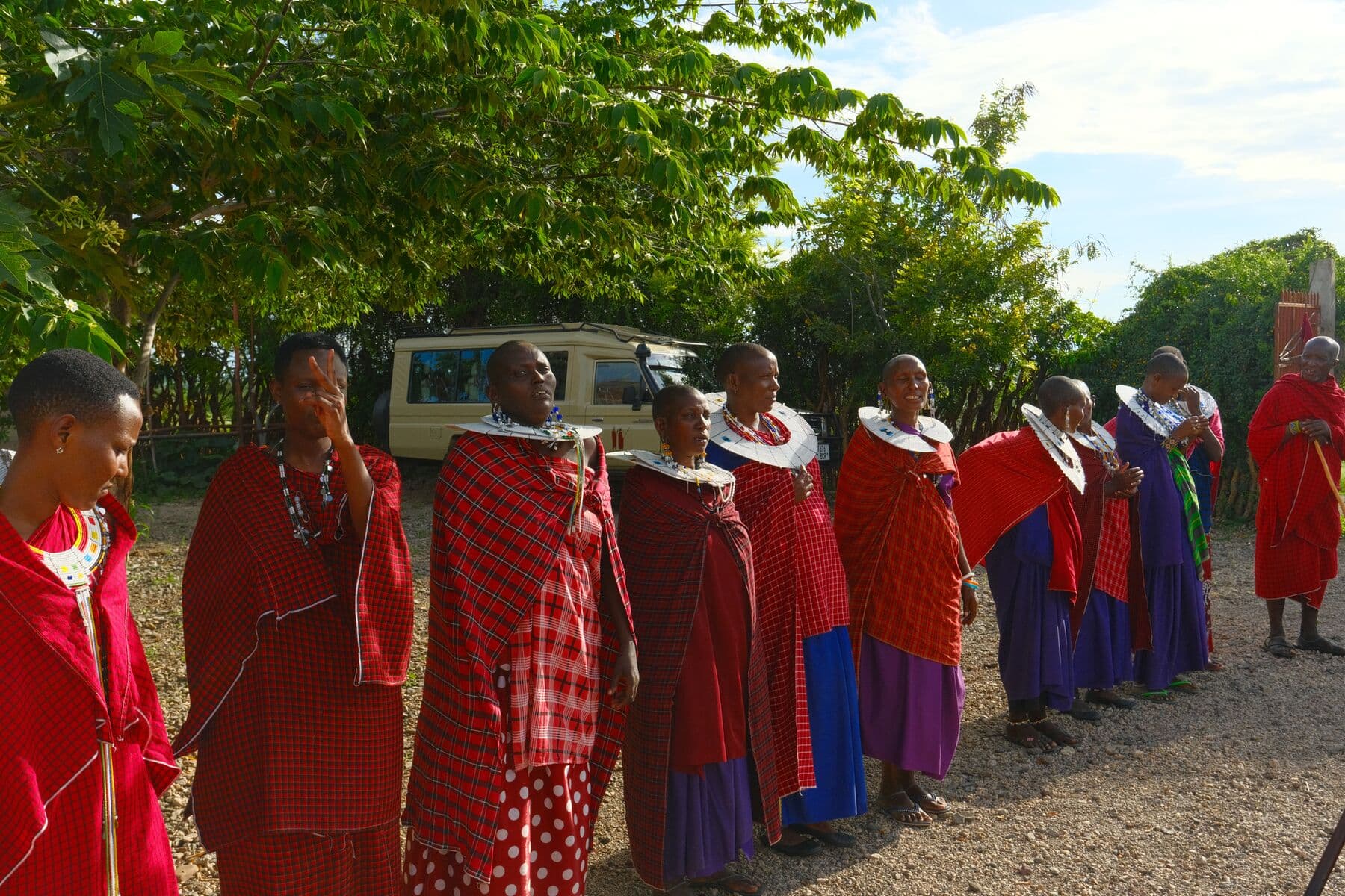 A group of Maasai women in red and blue shukas gathered beside a safari vehicle.